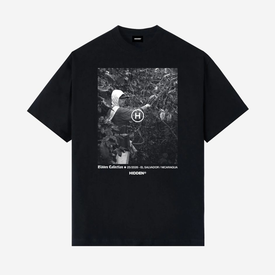 Vista delantera de camiseta negra Hidden Collection con fotografía en blanco y negro de un recolector de café entre plantas, y texto "El Salvador / Nicaragua"
